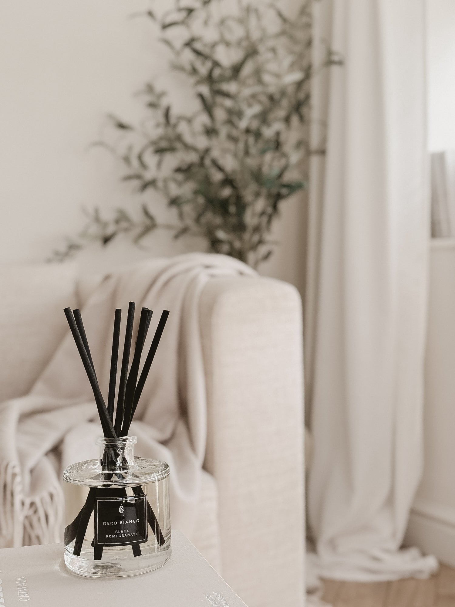 Black Pomegranate Reed Diffuser with black reed on a white surface with an olive tree in the background