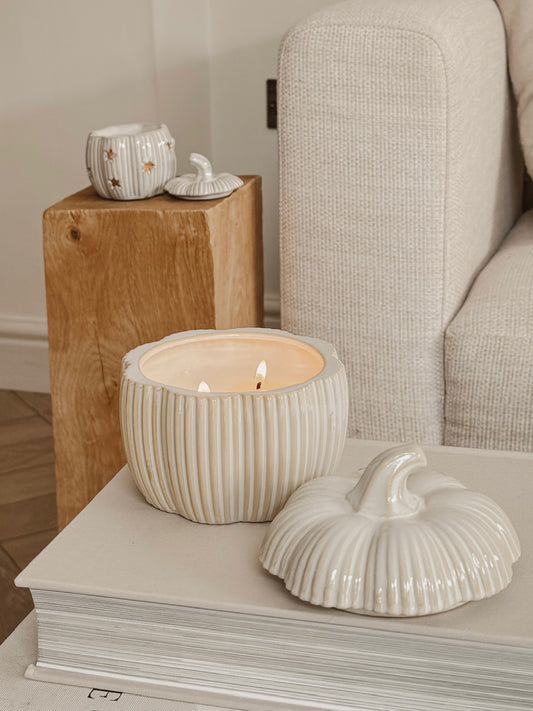 Ceramic pumpkin candle holder with ribbed texture on a surface, surrounded by neutral-toned decor.