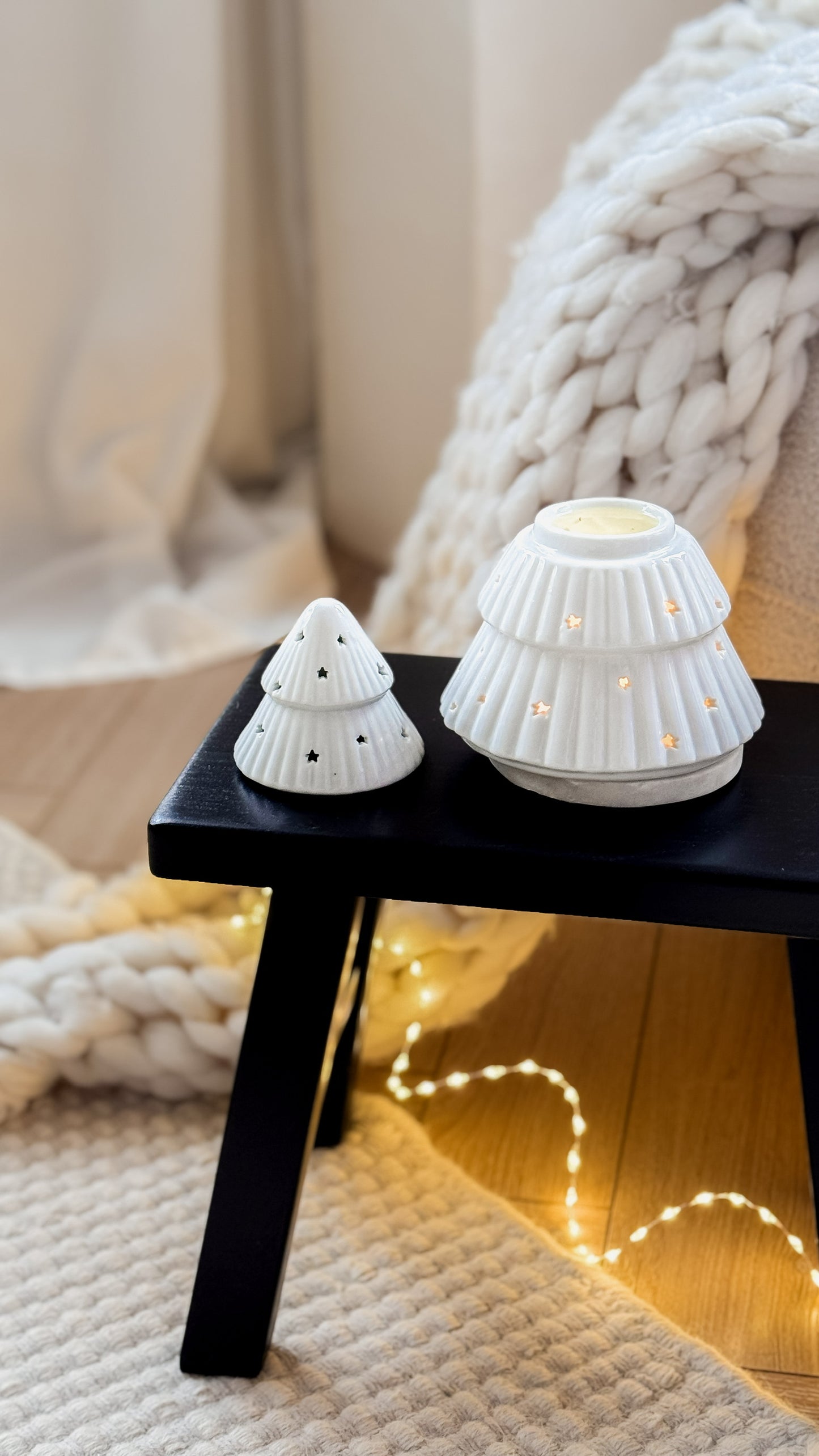 Two white ceramic tree-shaped lamps on a black stool with soft lighting and cozy background