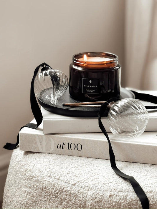 A dual wick candle with an amber glass vessel and a black lid, placed on top of a book, with its wick visible and a black ribbon nearby.
