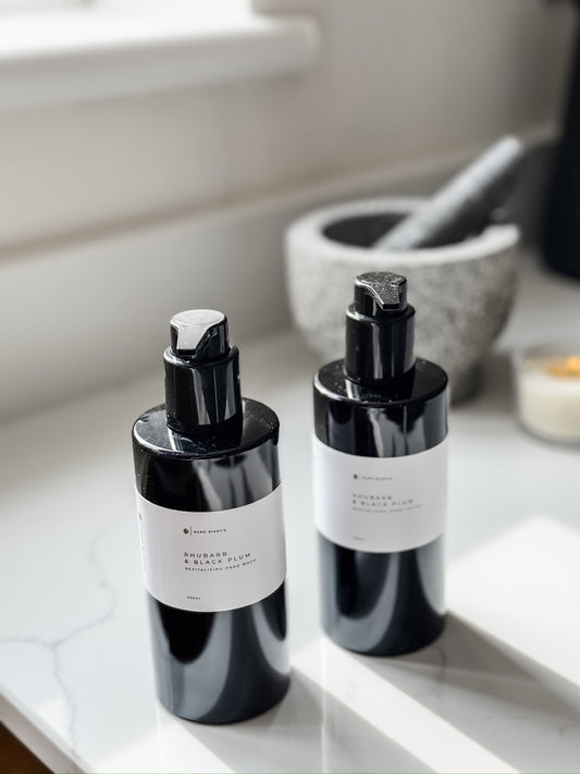 Luxury hand wash and hand lotion black bottles with white labels on a marble surface.