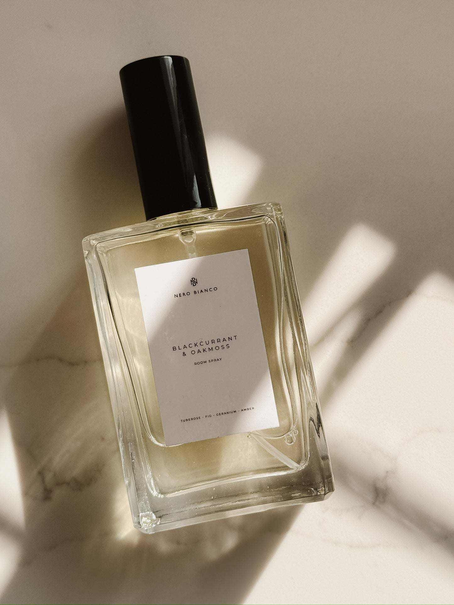 luxury room spray bottle with a black cap on a light marble background
