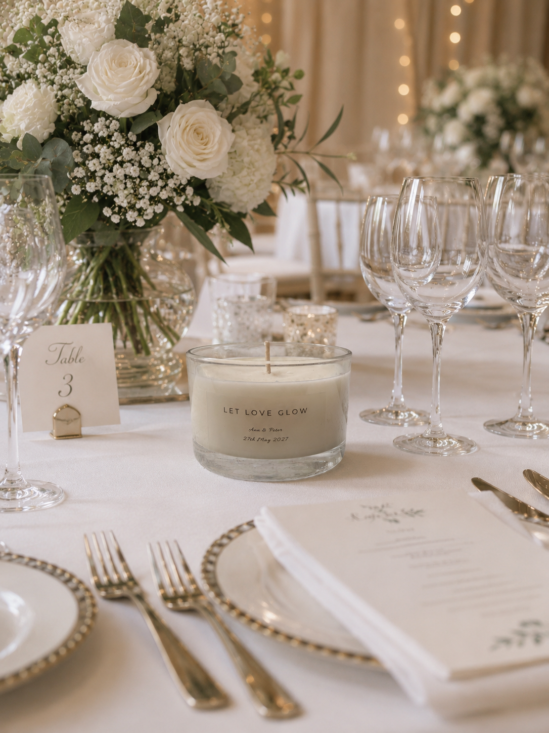 Elegant table setting with a candle, flowers, and cutlery on a white tablecloth.