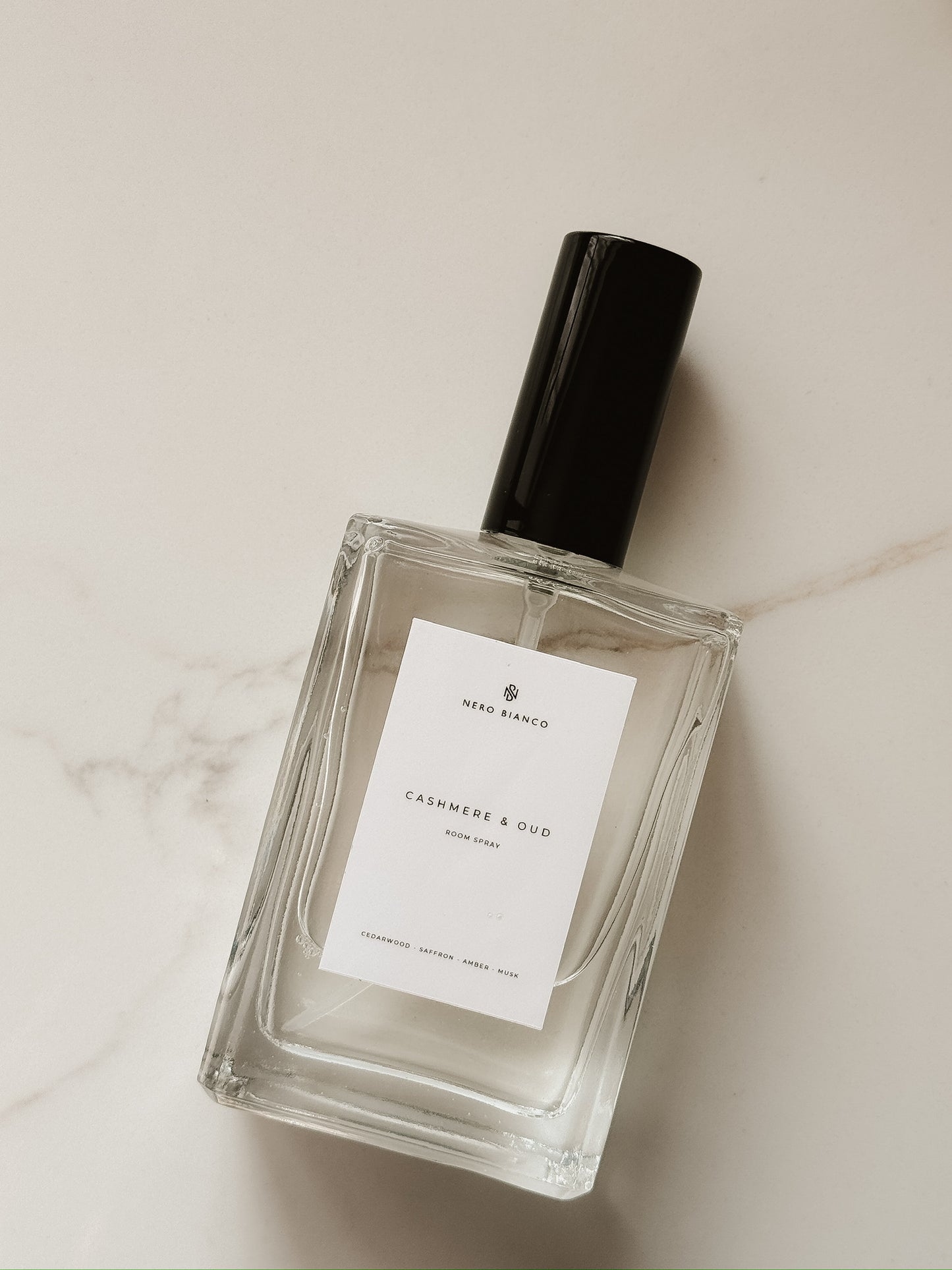 room spray in glass bottle with a black cap on a light marble surface