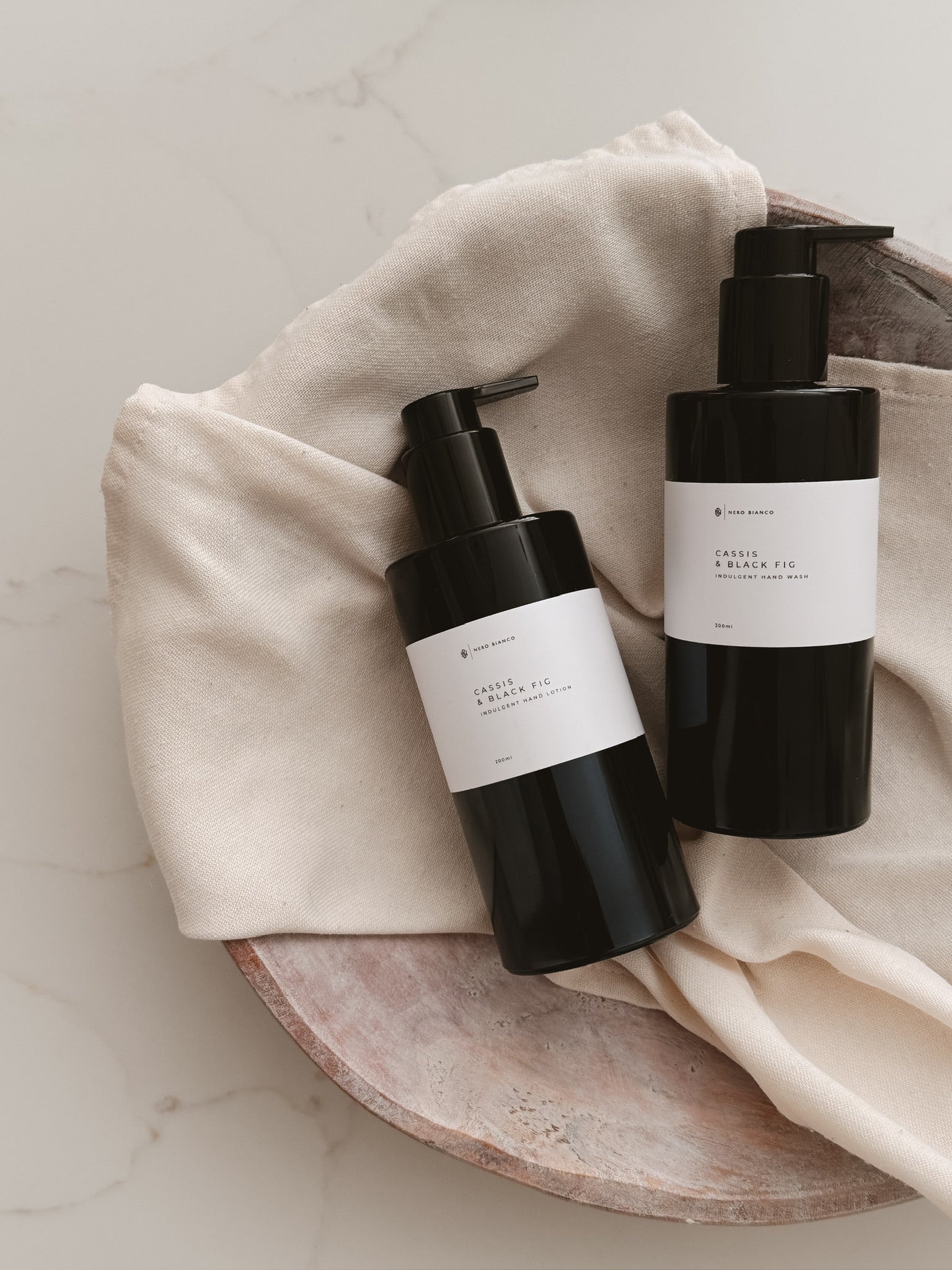 hand wash and hand lotion in black bottles with white labels on a beige towel and plate