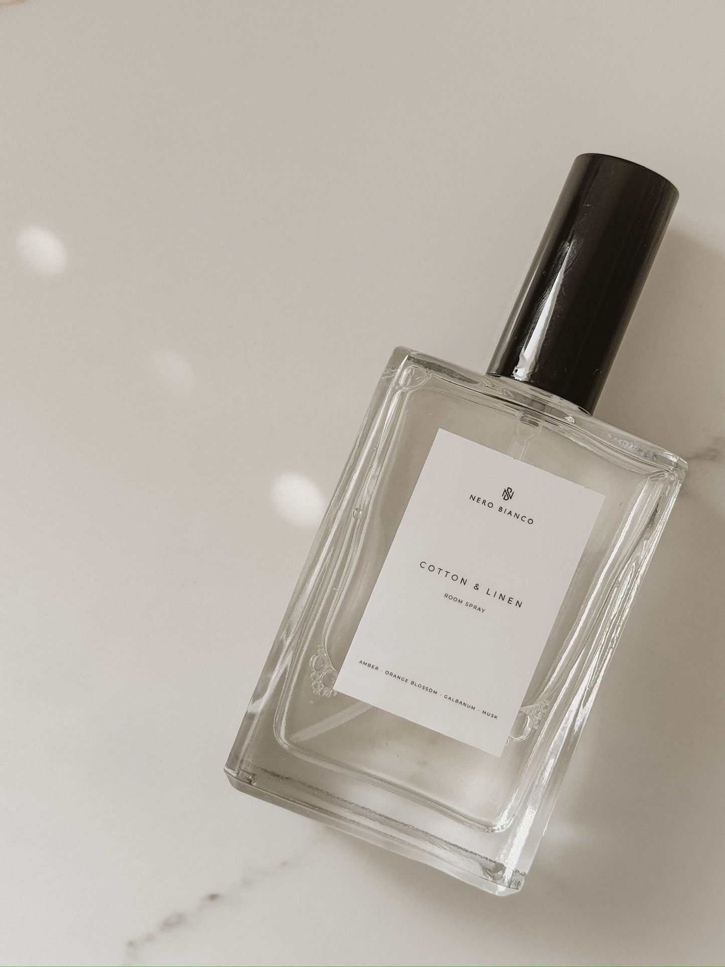cotton and linen room spray in glass bottle with black cap on a light gray background
