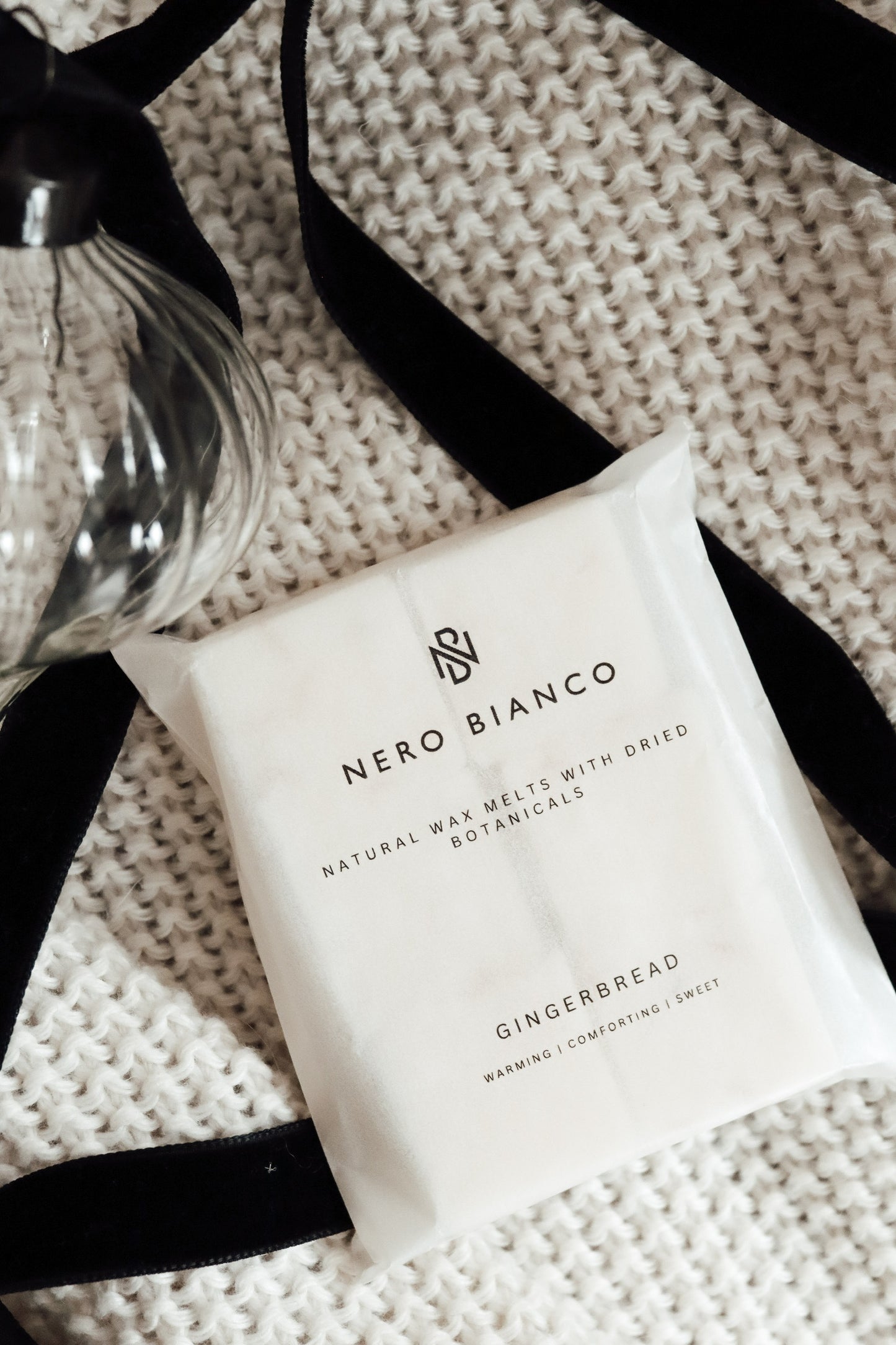 gingerbread scented wax melts lying on a beige blanket with a glass bauble and black ribbon