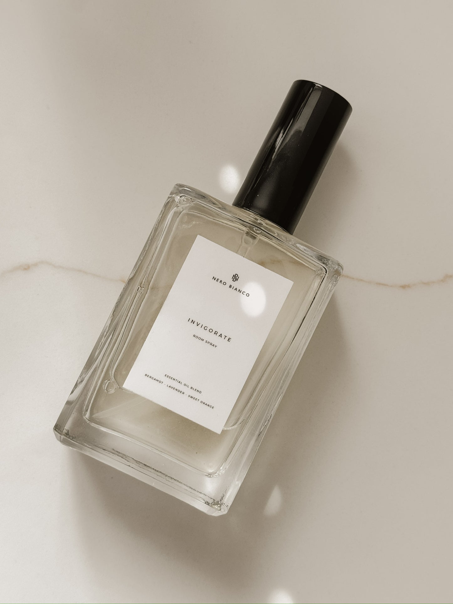 invigorate essential oil room spray in glass bottle with black cap on a marble surface