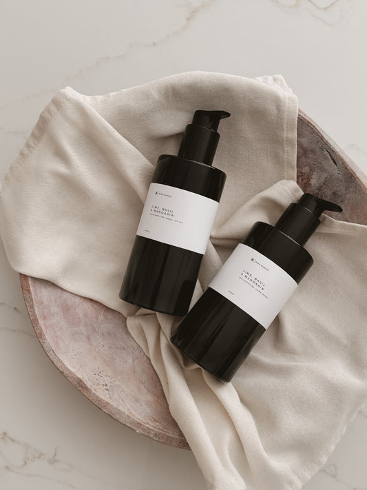 hand wash and hand lotion in black pump bottles with white labels on a beige cloth.