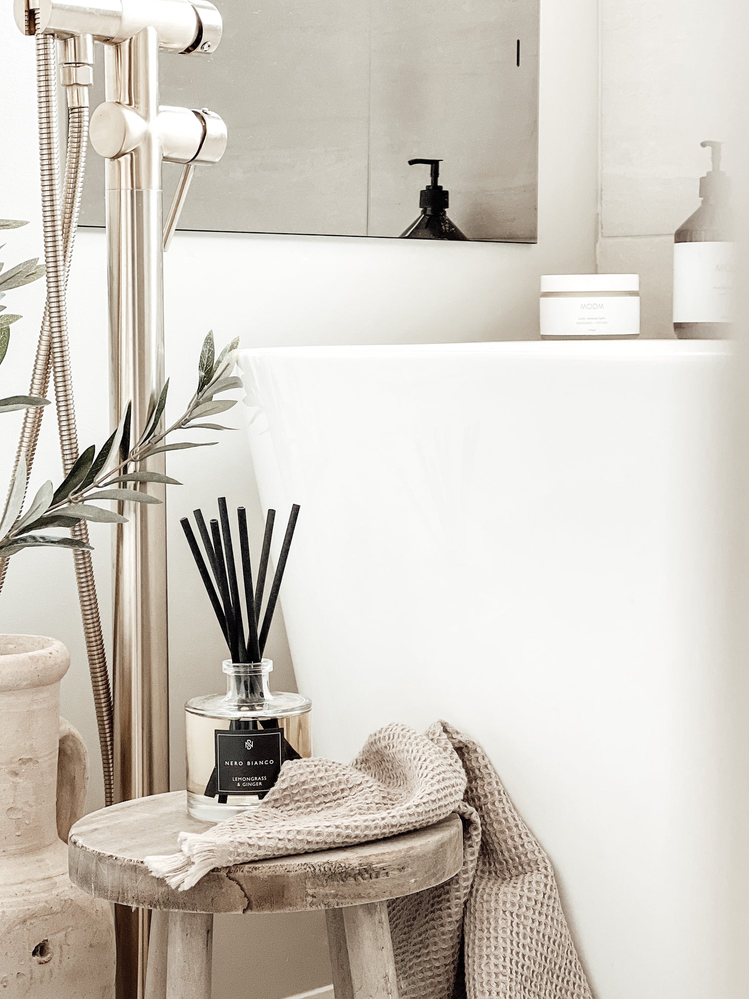 Signature Reed Diffuser lemongrass and ginger with black reeds in neutral bathroom styled on wooden milking stool