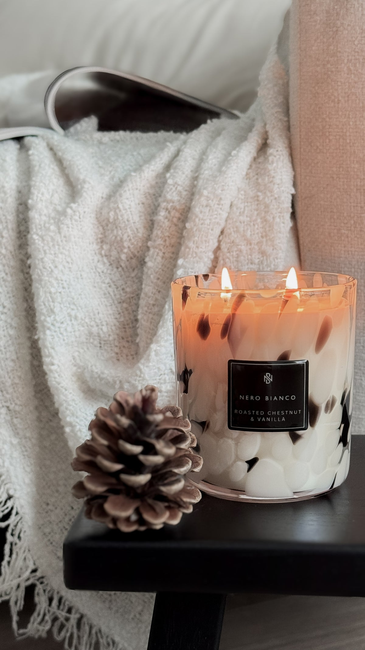 Dalmatian print candle with roasted chestnut & vanilla label on a table next to a pine cone, with a blanket in the background