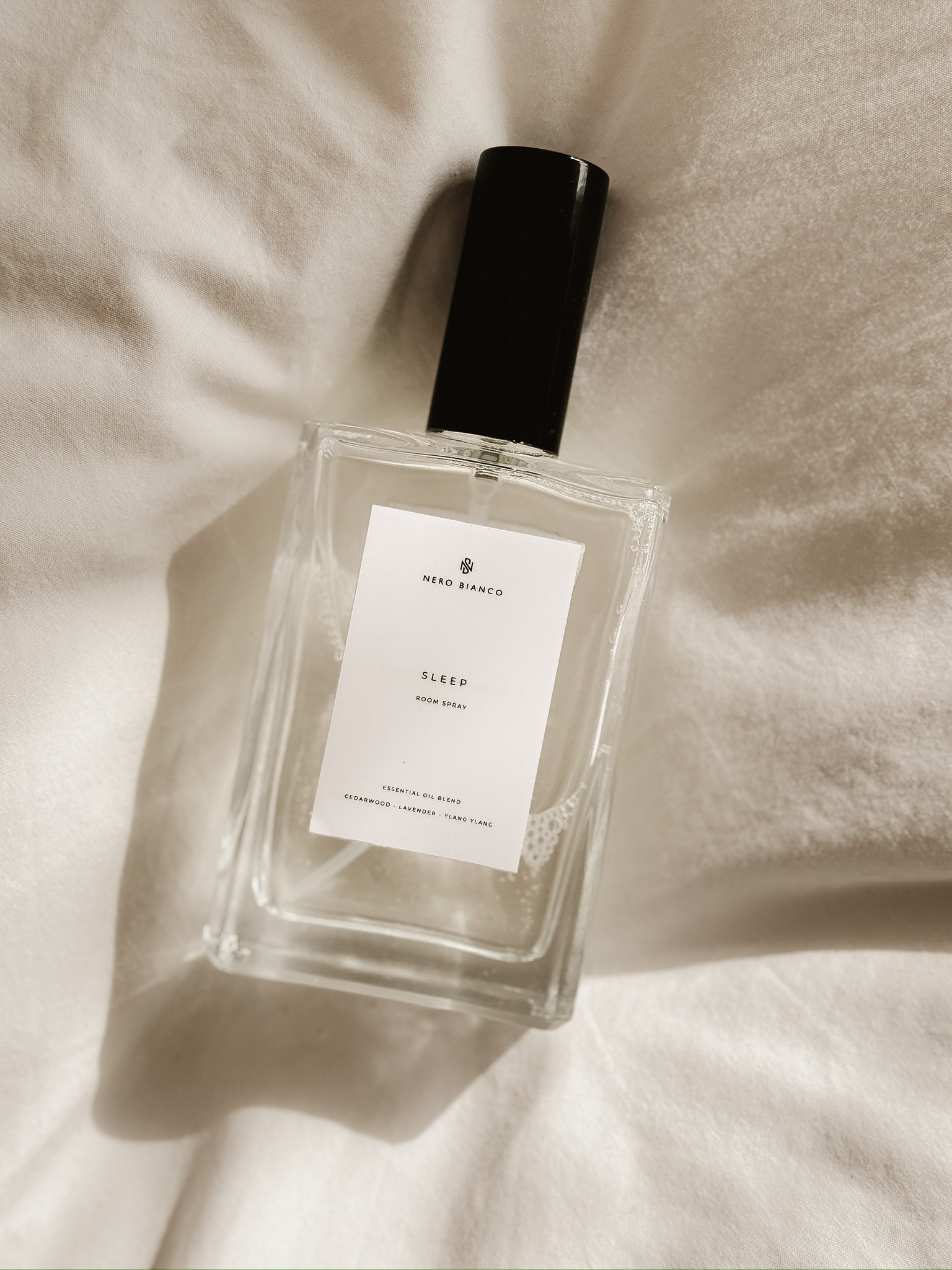 sleep room spray in rectangle glass bottle with black lid on light bedding