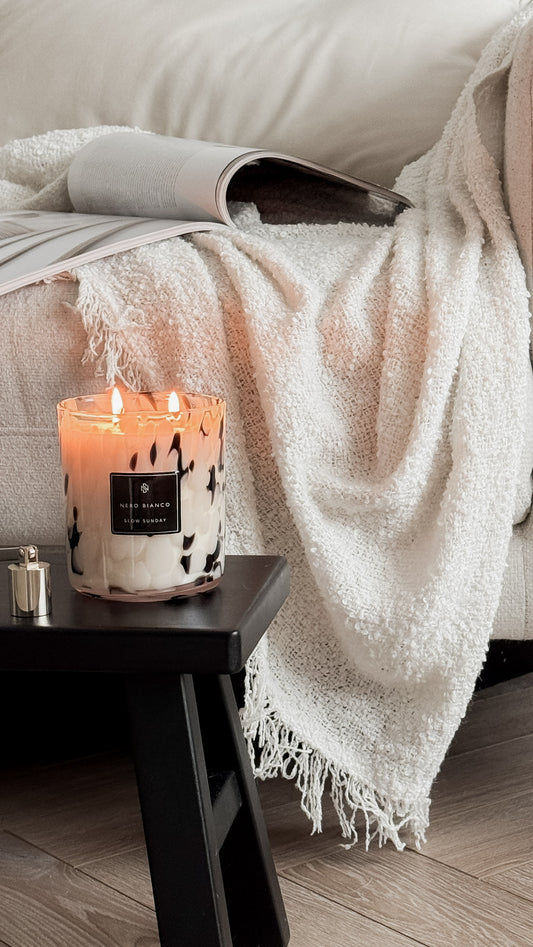 Candle on a small table next to a sofa with a blanket draped over it