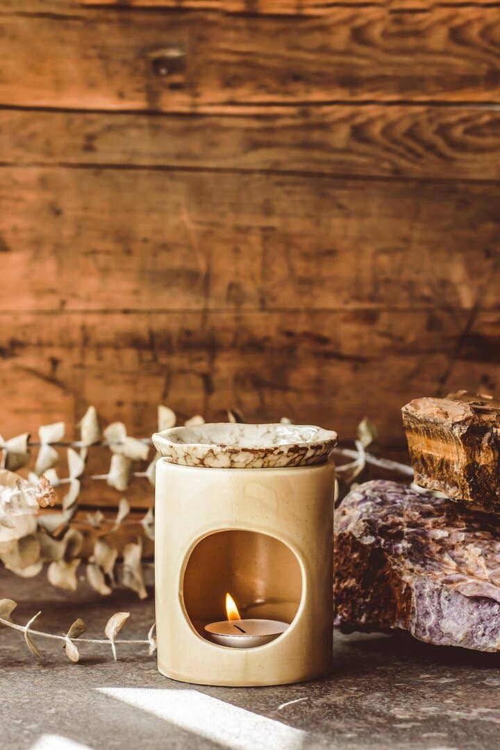Ceramic oil and wax melt burner with a lit candle on a wooden surface with a rustic background