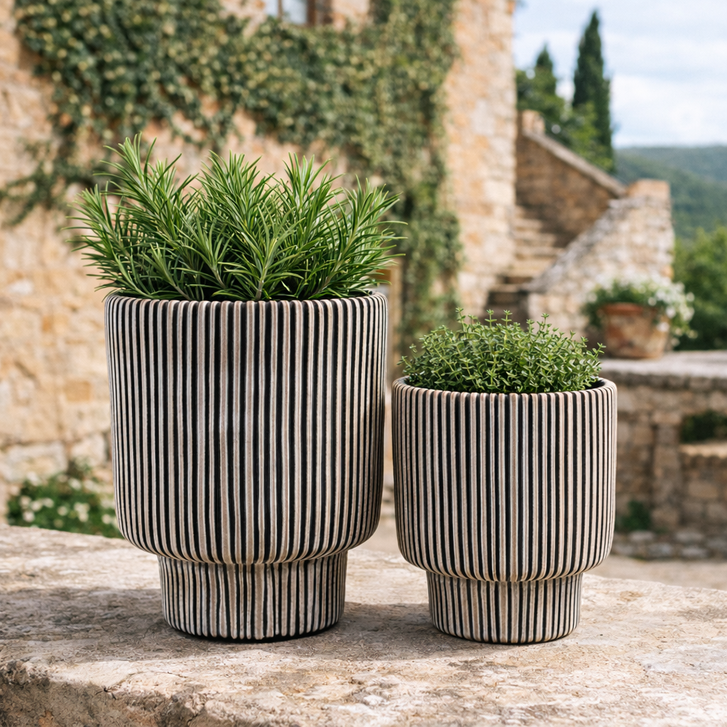 Two striped ceramic planters with green plants on a stone ledge.