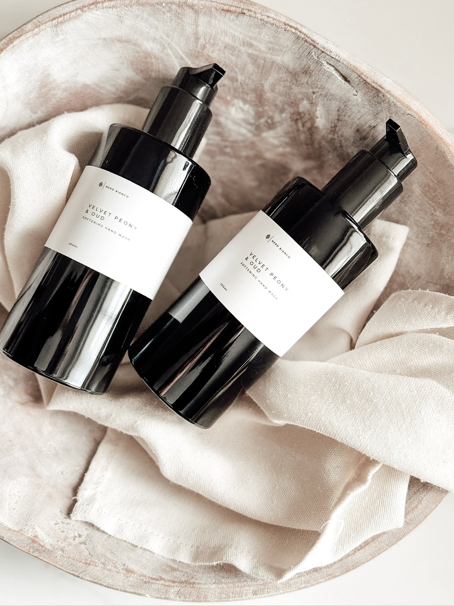 Two black skincare bottles with white labels on a beige fabric background