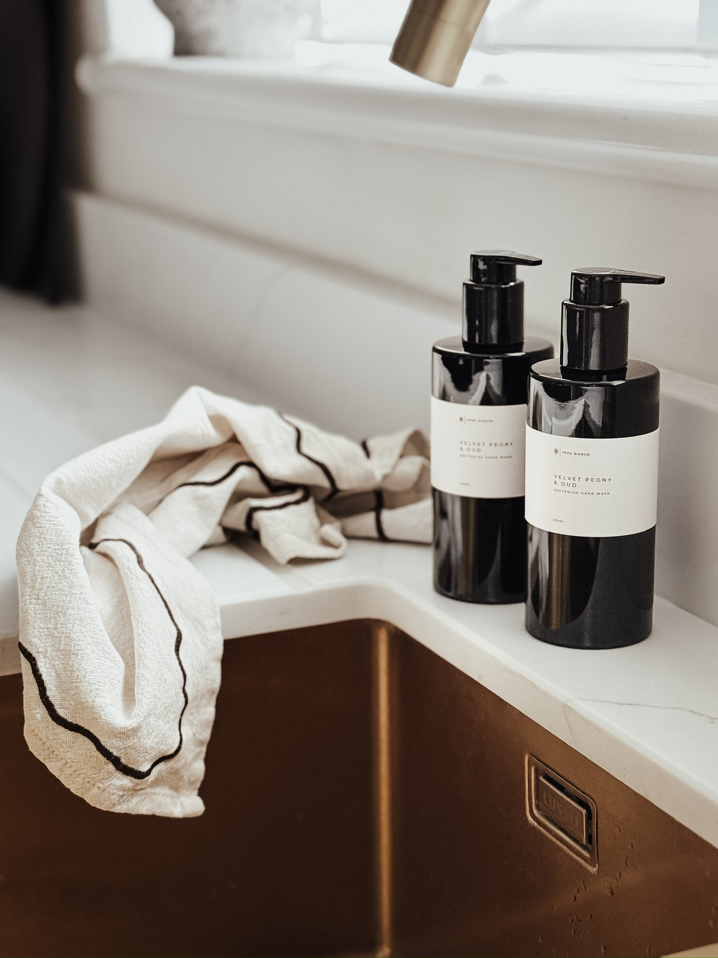 Two black bottles with pump dispensers on a bathroom counter next to a towel.