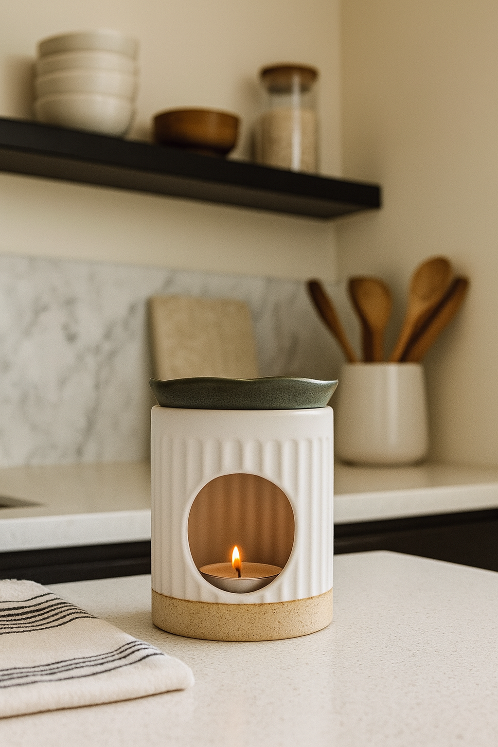 Ceramic white and olive wax melt burner with a lit candle on a kitchen counter
