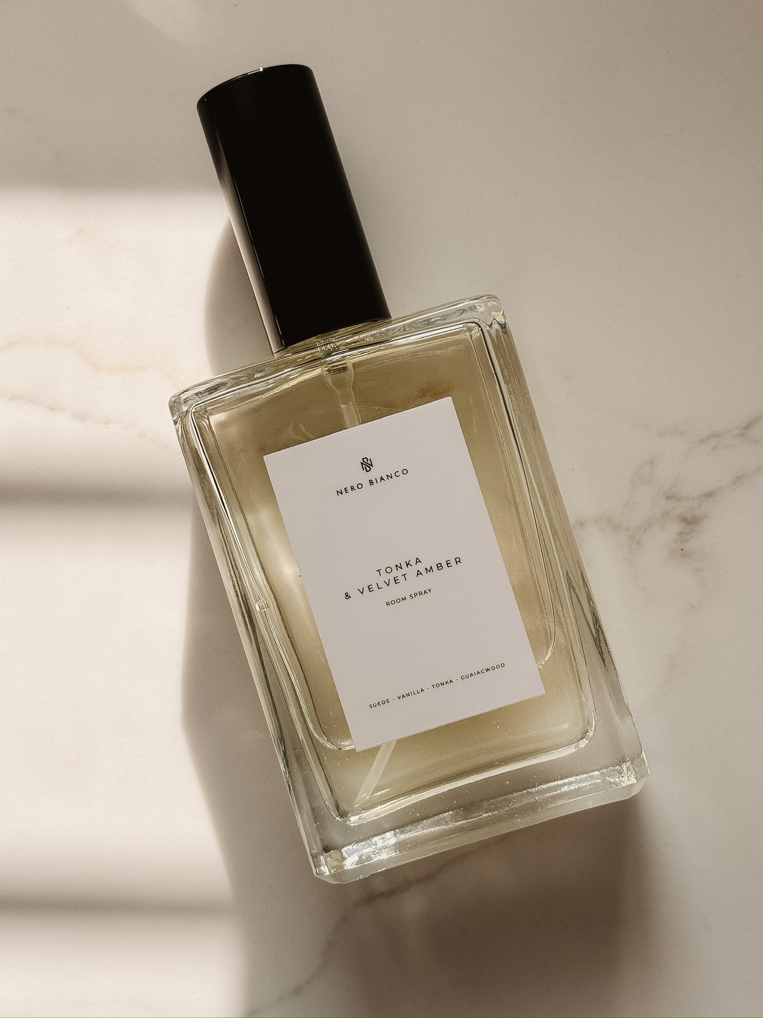 room spray in a glass bottle with a white label lying on a marble surface