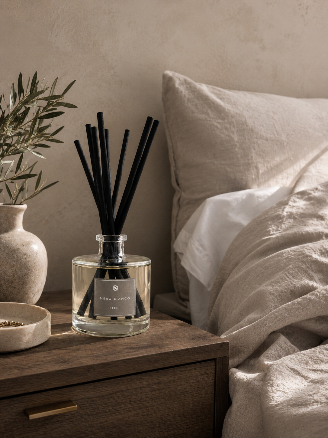 Diffuser on a bedside table with a bed and plant in the background