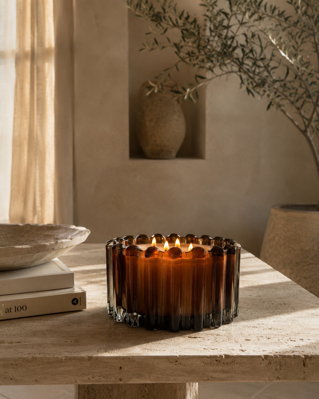 An amber glass candle holder with a lit candle, styled on a stone table in a warm, rustic interior setting.