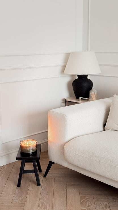White sofa with a black lamp and candle on a wooden floor in a minimalistic room.