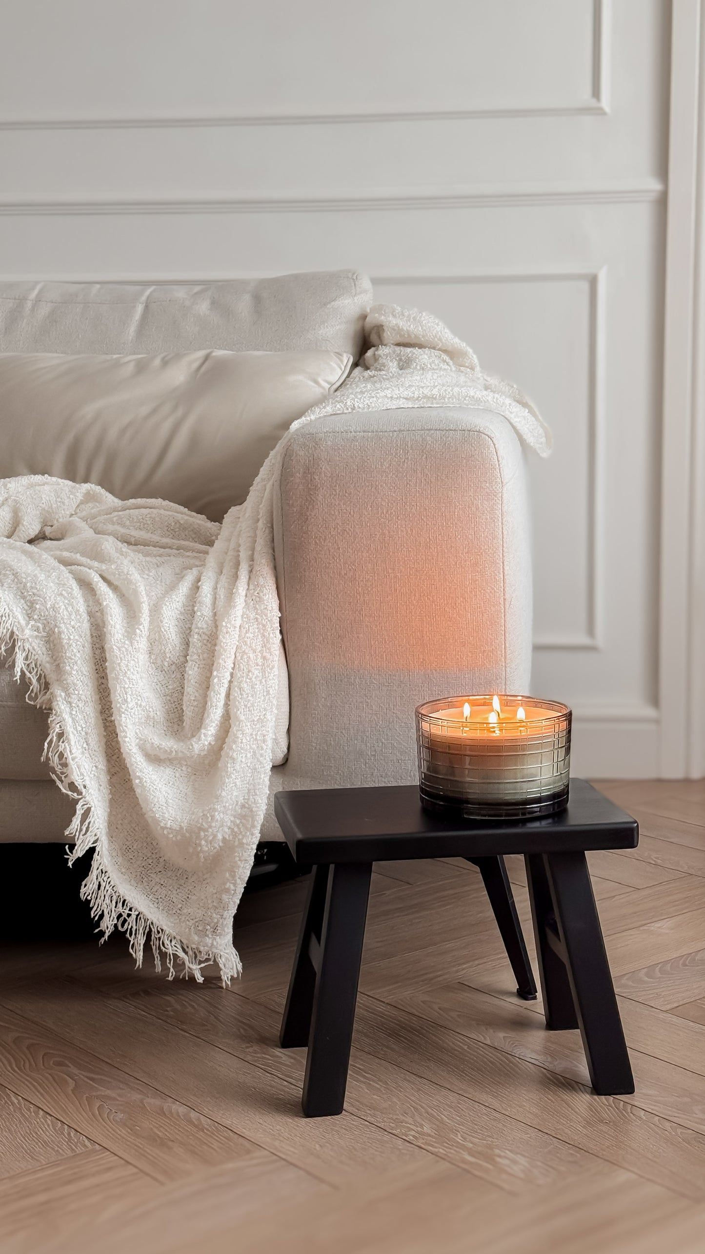 Candle on a small wooden table next to a beige sofa with a white blanket.