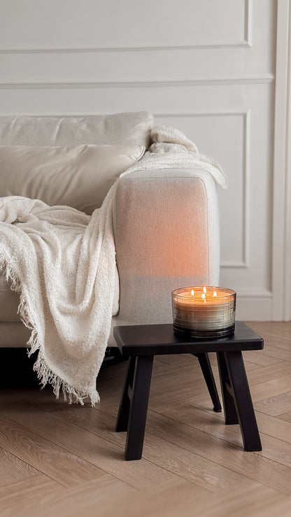 Candle on a small wooden table next to a beige sofa with a white blanket.