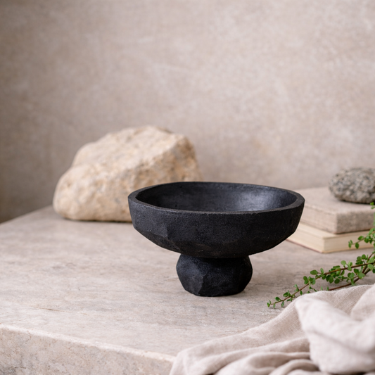 Black stone bowl on a neutral surface with a rock and books in the background