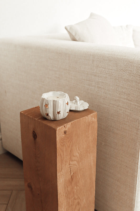 Small ceramic pumpkin wax melt burner on a wooden block in front of a beige sofa