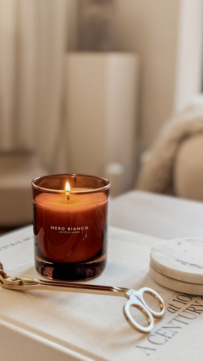 Nero Bianco candle in a glass jar on a table with wick trimmer and coasters.