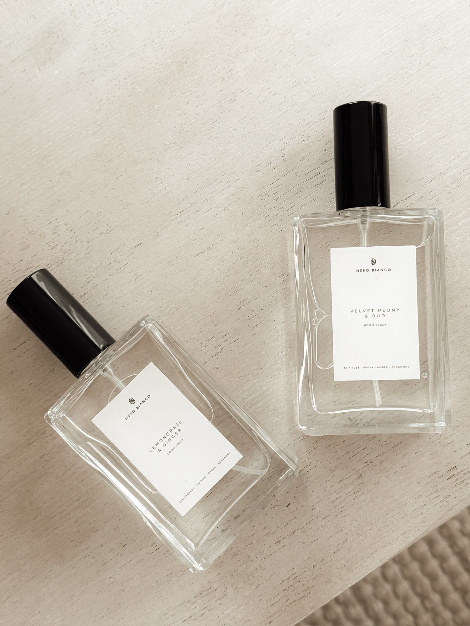Two clear room spray bottles with black caps on a textured beige surface