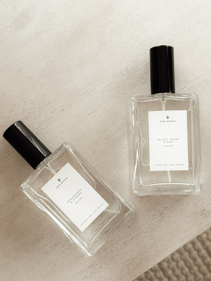 Two clear room spray bottles with black caps on a textured beige surface