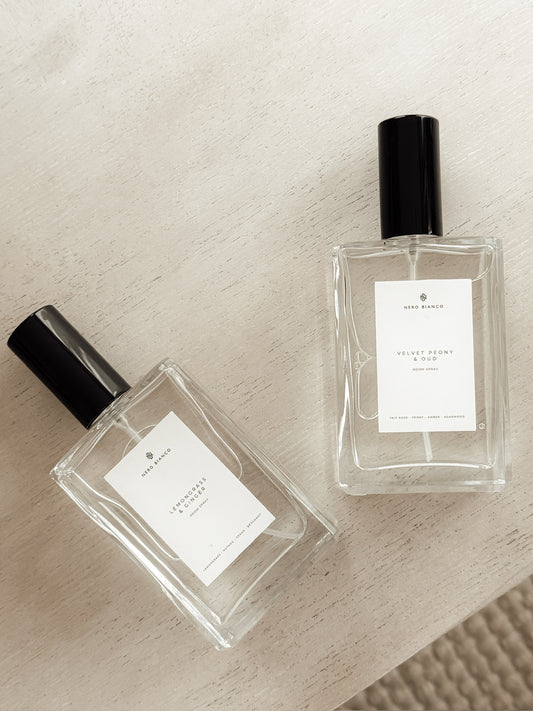 Two clear room spray bottles with black caps on a textured beige surface