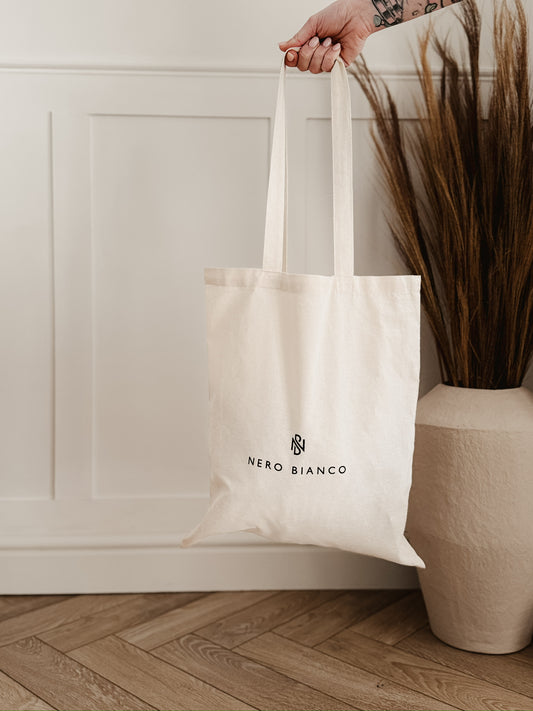 White tote bag with Nero Bianco logo held by a hand against a neutral background