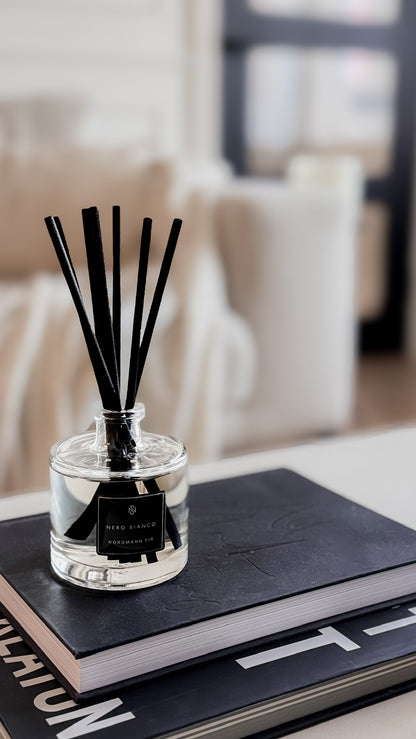 Reed diffuser with black sticks in a clear container on a book