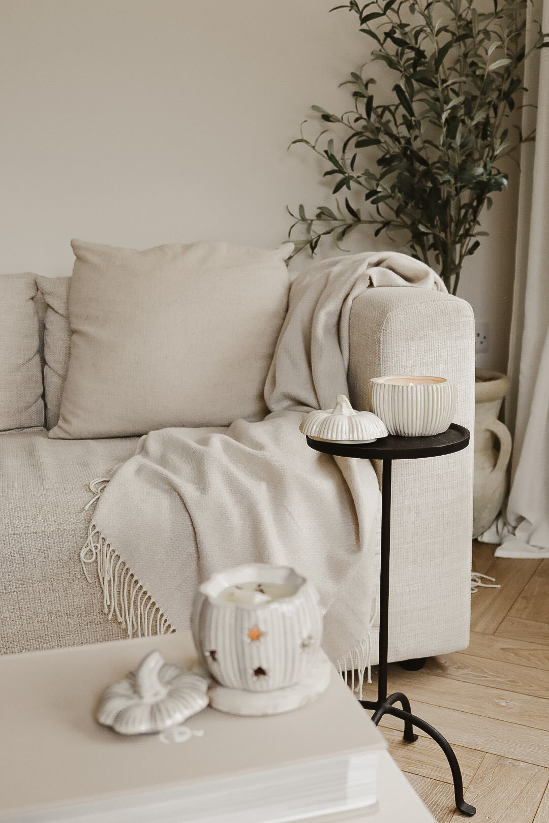 PUMPKIN CANDLE AND PUMPKIN WAX MELT BURNER IN A NEUTRAL LIVING ROOM WITH OLIVE TREE
