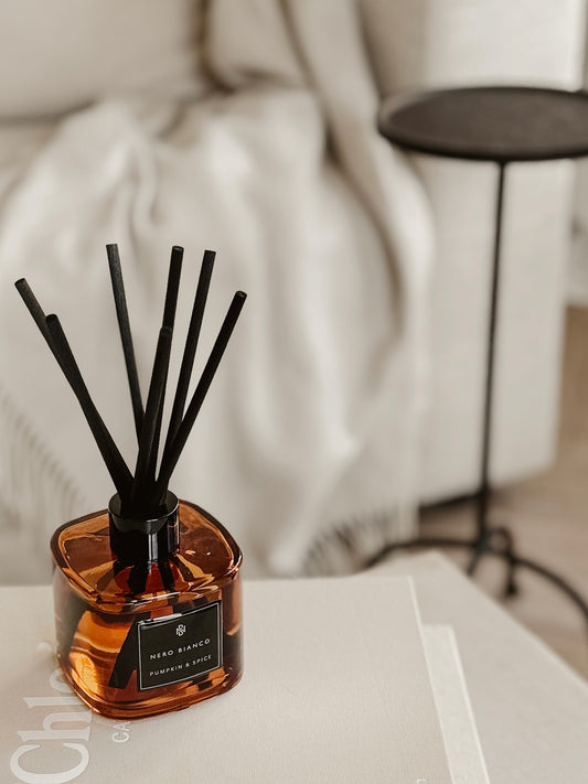 Reed diffuser with black reeds in an amber glass bottle on a blurred background
