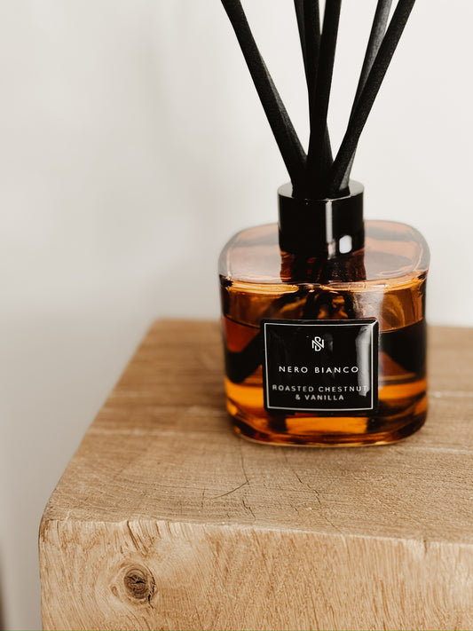 Amber glass reed diffuser sitting on wooden surface