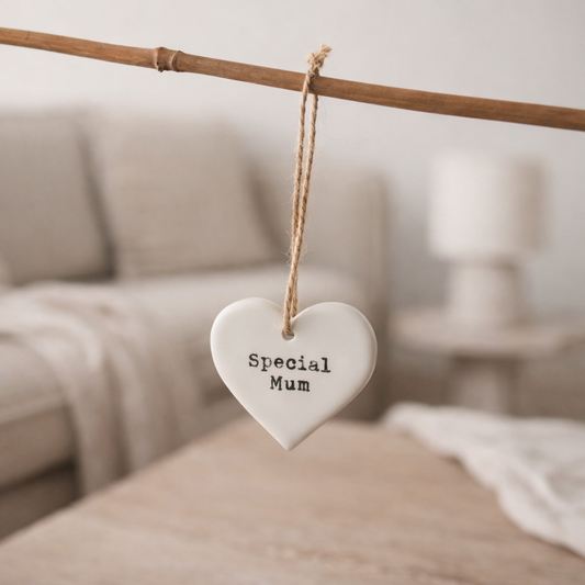 Heart-shaped ceramic ornament with 'Special Mum' text hanging on a branch in a blurred indoor setting.