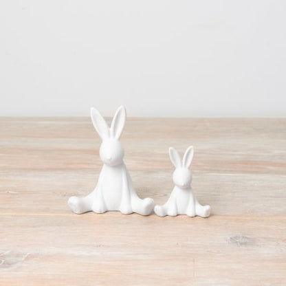 Two ceramic figurines of bunnies in different sizes with a textured surface, placed on a wooden surface.