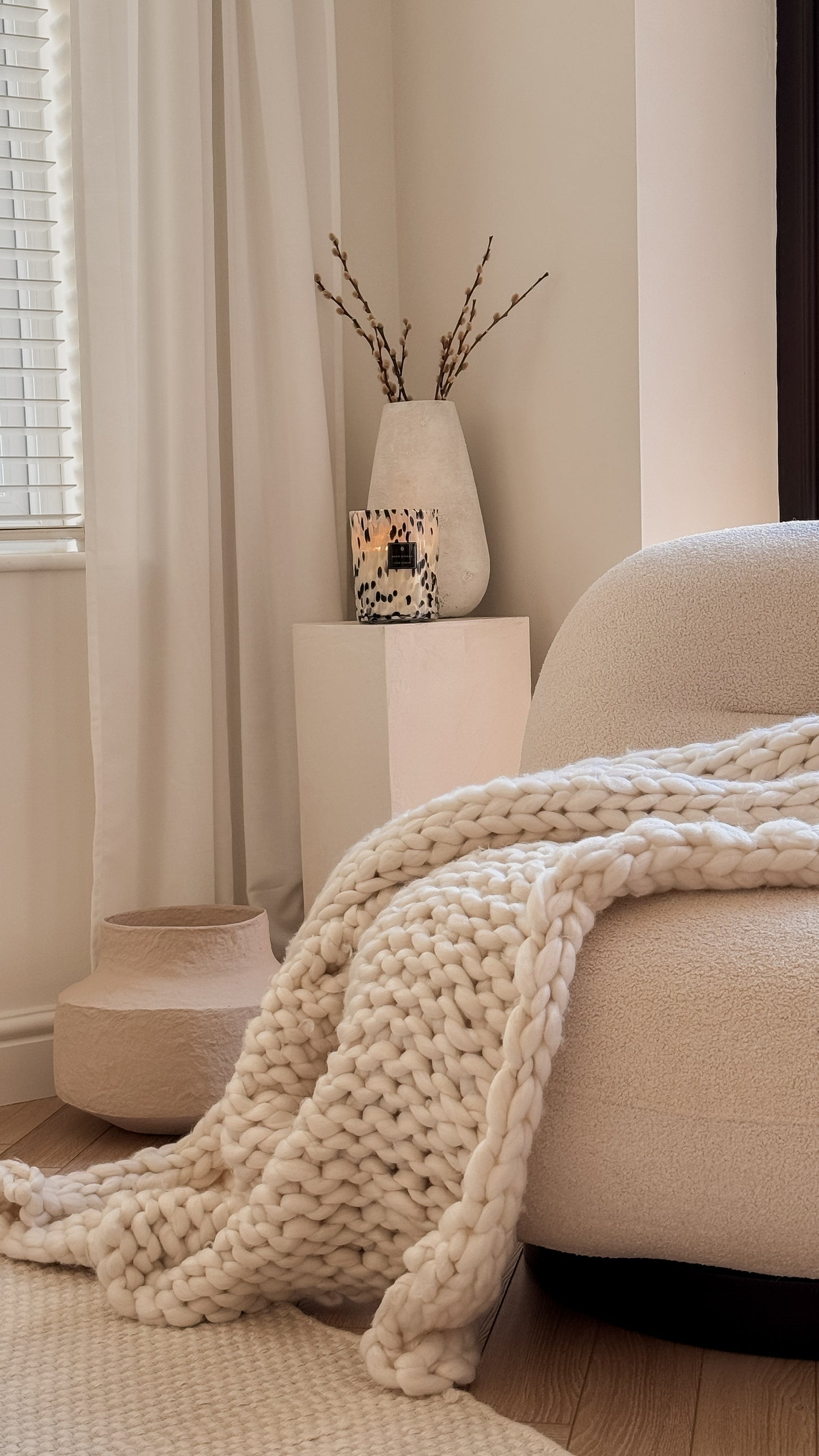 Cozy living room with beige sofa, chunky knit blanket, and decorative elements.
