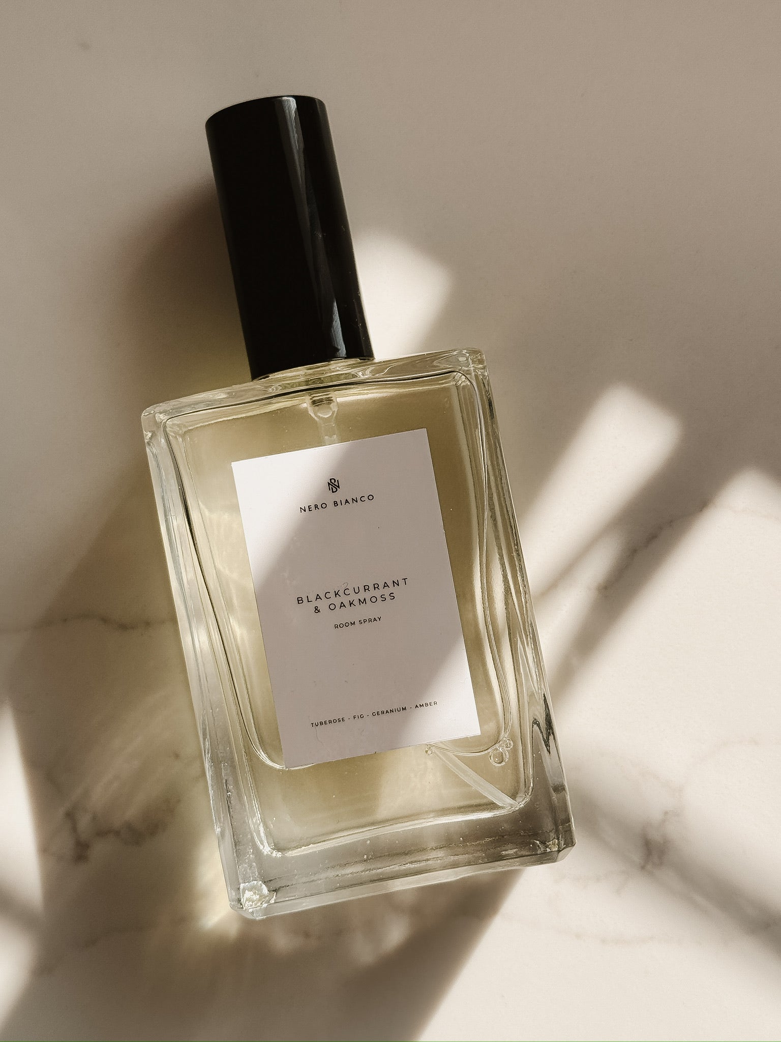 luxury room spray bottle with a black cap on a light marble background