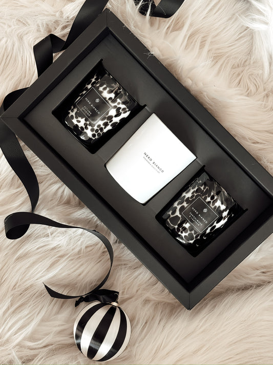 A trio of candles in black and white packaging with a leopard print design, displayed on a furry surface with a black ribbon.