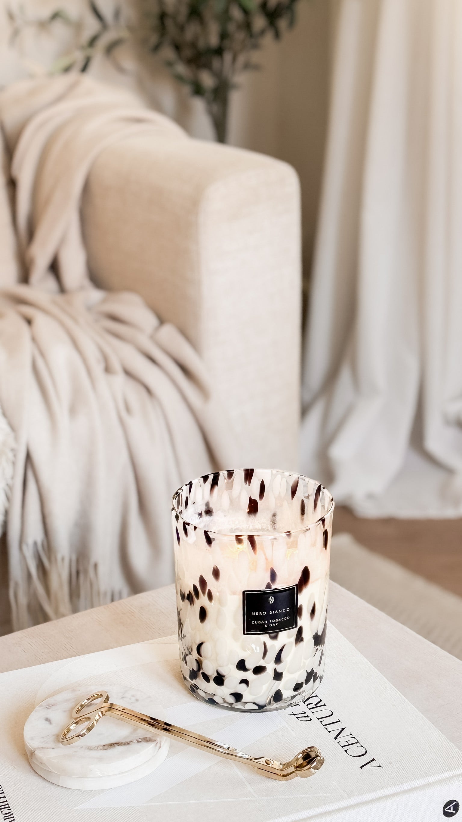 Candle with a dalmatian print on a table next to a blanket and gold wick trimmers