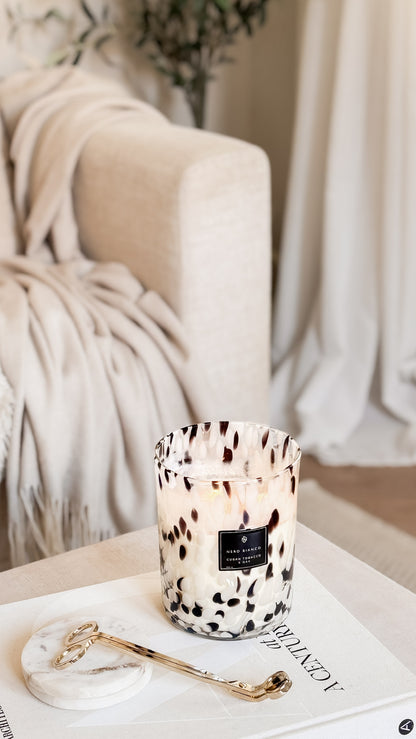 Candle with a dalmatian print on a table next to a blanket and gold wick trimmers