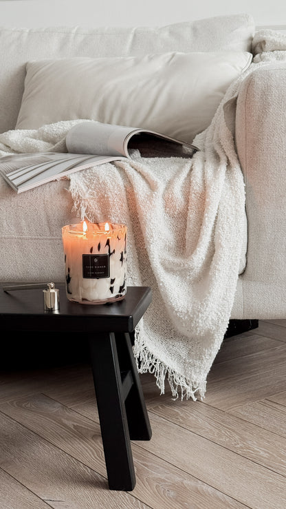 Candle on a small table in front of a beige sofa with a white blanket