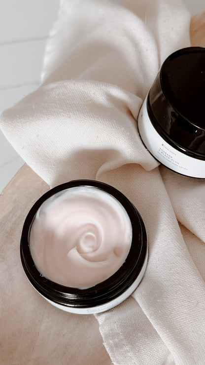 Two open jars of hand lotion on a light fabric background
