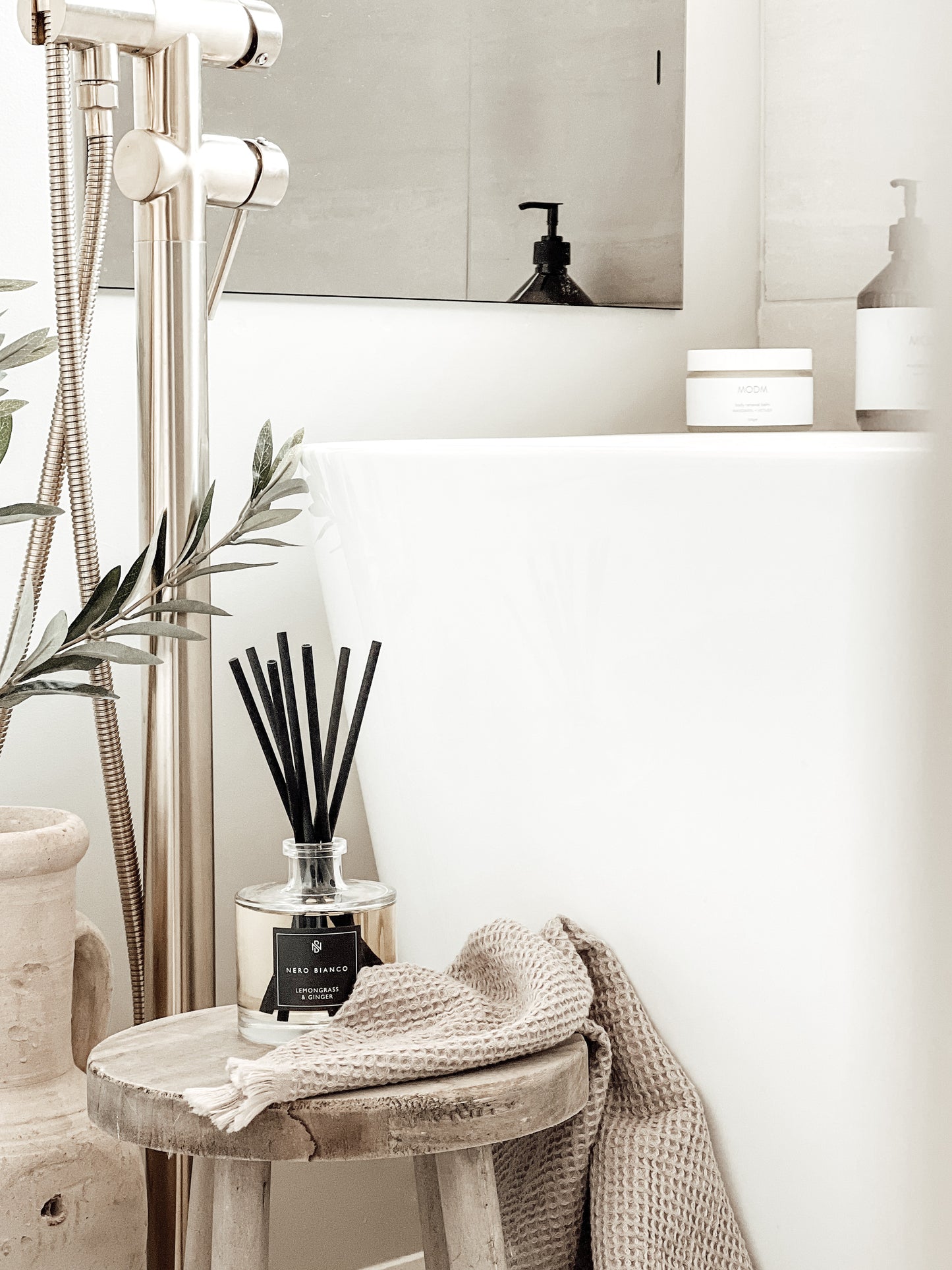 Signature Reed Diffuser lemongrass and ginger with black reeds in neutral bathroom styled on wooden milking stool