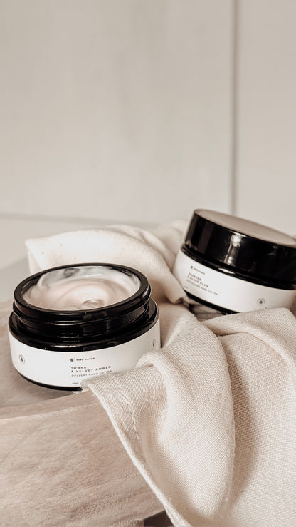 Two mini hand lotion jars on a light fabric background
